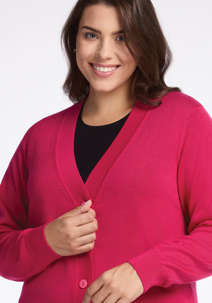 A person smiling, dressed in the Woolx Gia Sweater in Berry Burst over a black top, standing against a plain white background.