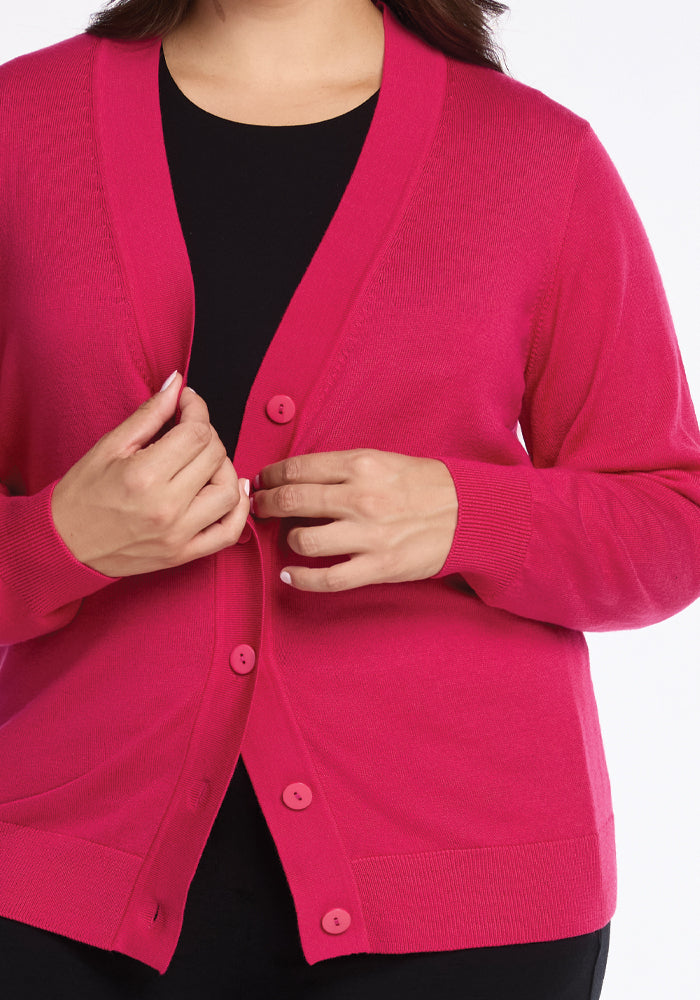 A person is depicted wearing the Gia Sweater in Berry Burst from Woolx over a black top. The sweater features buttons down the front, and the person is adjusting it with their hands. Only the torso and arms are visible against a white background.