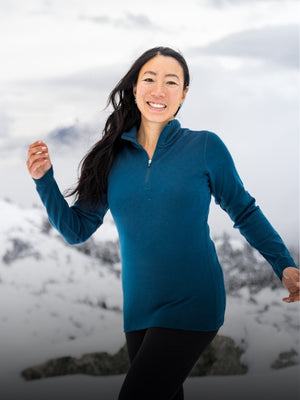 Model wearing Real Teal Brooke 1/4 zip top while standing in front of snowy mountain range mobile size