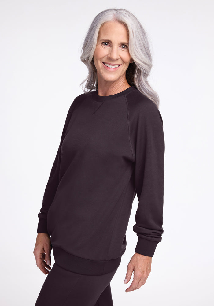 A smiling woman with long gray hair wearing a Bailey Crewneck Sweatshirt in Chocolate Plum from Woolx stands against a plain white background.