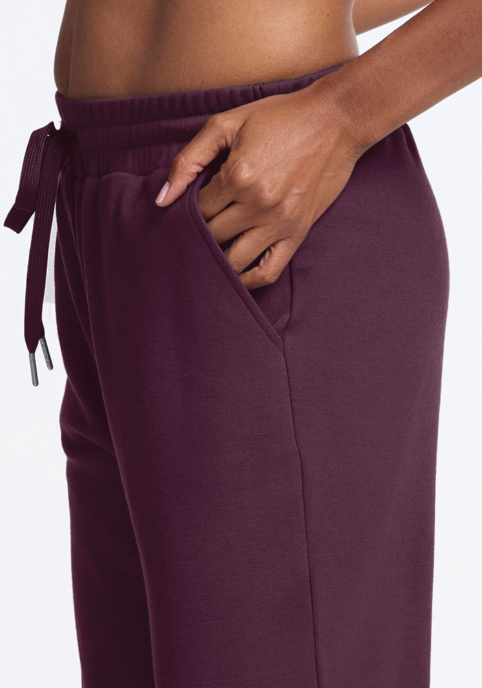 A person wearing Woolx's Parker Sweatpants in Wine Tasting with one hand in the pocket. These temperature-regulating pants feature a drawstring waistband and a relaxed fit. The background is plain white.