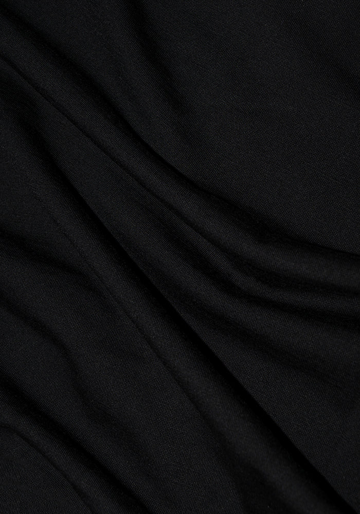 A close-up of the Elena V Neck in black from Woolx reveals its soft, smooth Merino wool fabric with gentle folds. The slightly stretchy material captures light to highlight subtle creases, delivering a rich, deep look that encapsulates casual chic.