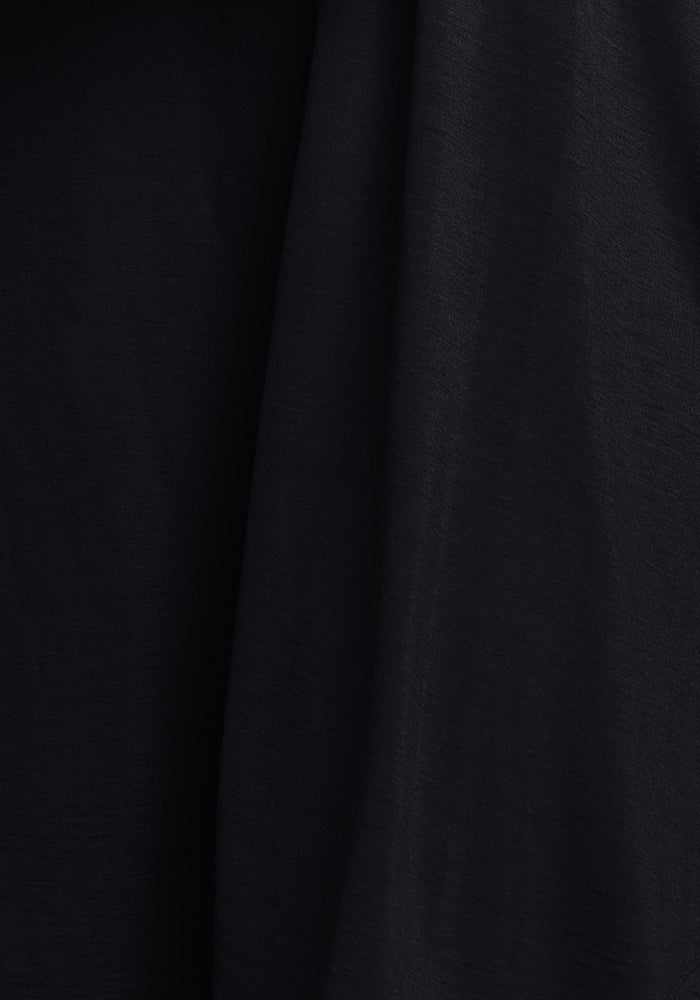 A close-up of the Billie Lounge Tee - Black by Woolx, crafted from Merino wool fabric that boasts a soft texture and gentle wrinkles, forming delicate waves in the material. The lighting accentuates the moisture-wicking shades and folds, adding depth to the image.