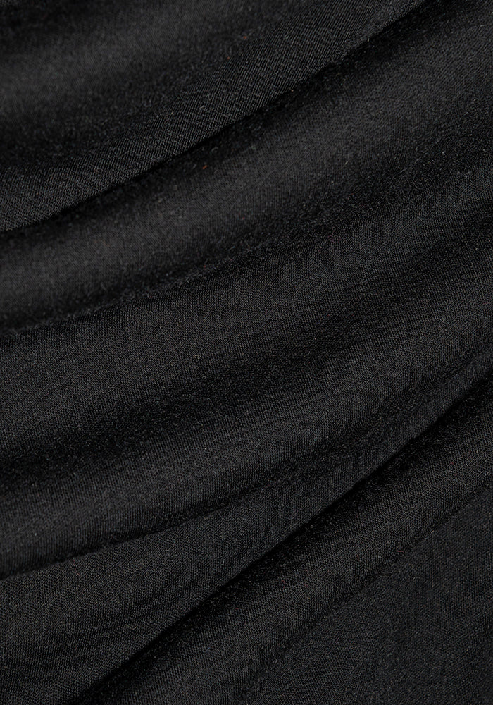 Close-up of the Woolx Sophia Bodysuit in black fabric, draped in soft, flowing folds. The texture appears smooth and slightly shiny, creating gentle curves and shadows that perfect a chic look.