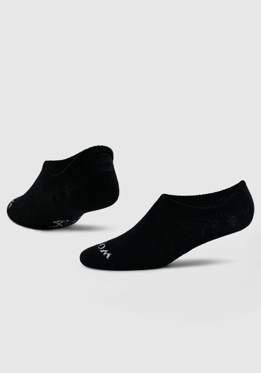 Two Daisy Ped Socks - Black by Woolx against a plain background, with one sock slightly elevated and angled to showcase its shape. Subtle white text is visible near the toes of each sock.