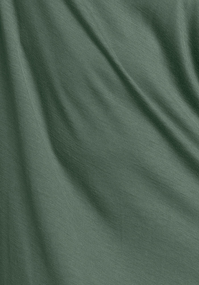 A close-up of the Billie Lounge Tee in Duck Green, crafted by Woolx, highlights its smooth texture and soft folds. The dark green merino wool fabric appears slightly shiny, enriched with moisture-wicking and odor-resistant properties, while natural creases create subtle shadows.