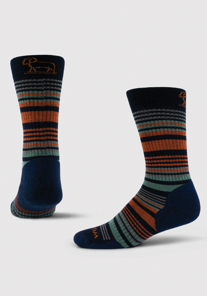 Two pairs of the "Everyday Crew Sock Light Cushion" by Woolx showcase stylish, durable designs with horizontal stripes in deep navy, orange, green, and gray. Made from moisture-wicking fabric, one sock stands upright while the other leans slightly to reveal a smaller embroidered ram's head near the top edge.