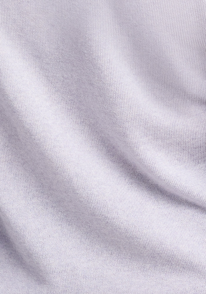 A close-up of the Francesca Sweater - Mist by Woolx reveals a textured white fabric with fine, evenly spaced knit patterns. The surface appears soft and smooth, with subtle folds and shadows enhancing its depth.