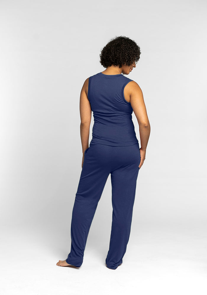 A person with curly hair stands barefoot, their back to the camera, wearing a travel-friendly Woolx Phoebe Lounge Tank in Starry Night and matching pants against a plain white background.