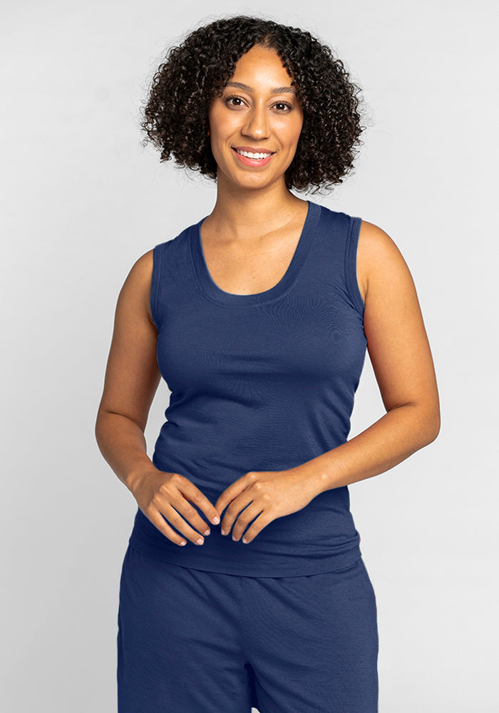 A person with curly hair, dressed in the Phoebe Lounge Tank - Starry Night by Woolx, featuring temperature-regulating Merino wool, smiles at the camera against a plain background, wearing matching navy blue pants.