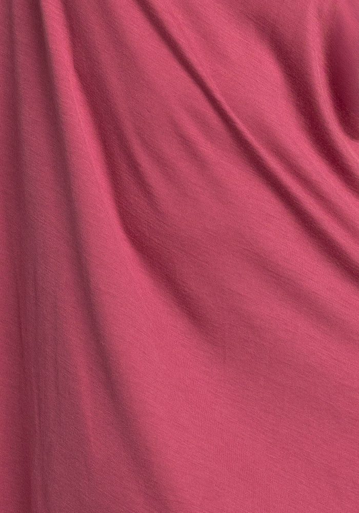 The Billie Lounge Tee in Red Violet by Woolx features a close-up of its pink moisture-wicking fabric, displaying soft, flowing folds. The smooth and slightly shiny texture reveals subtle shadows and highlights that add depth to the design.