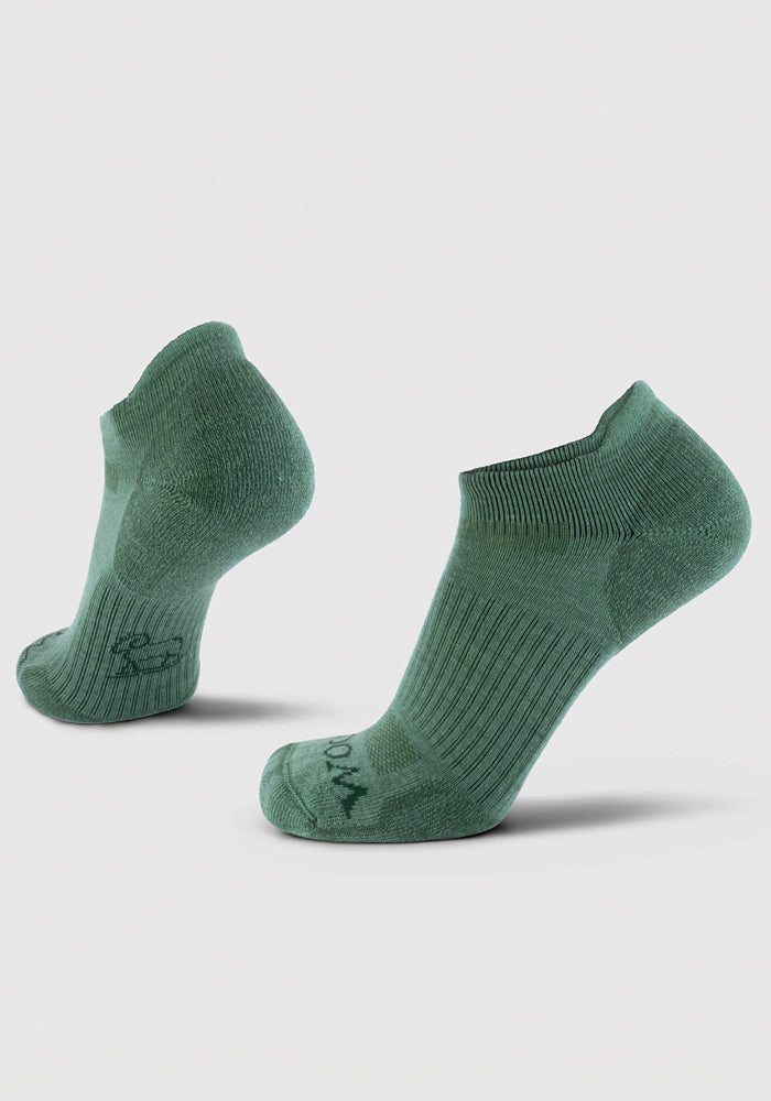 A pair of Rowan No Show Tab Lightweight Socks in Duck Green by Woolx, featuring a ribbed texture. Positioned upright against a light gray background, they showcase their arch support and heel design. The fabric is enhanced with antimicrobial technology and appears soft and stretchy.