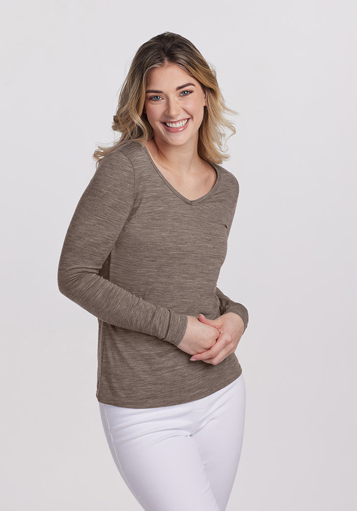 A person with long hair is smiling, wearing the Woolx Layla V Neck Top and white pants. They are standing against a plain white background.