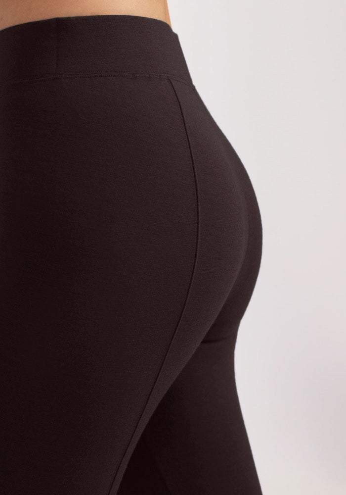 A close-up side view of a person wearing high-waisted, French Roast Woolx Stella Leggings. The image focuses on the lower back and upper leg area, highlighting the snug fit and smooth fabric of these cold weather baselayer leggings. The background is neutral and out of focus.