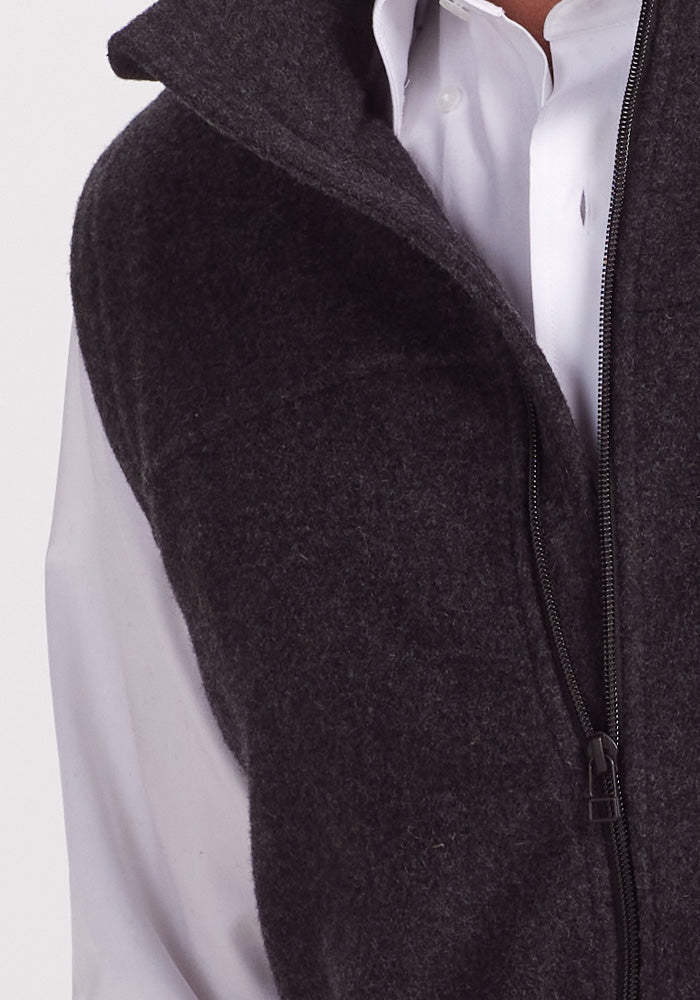 A person wearing a white button-up shirt and a Carbon Black Stowe Vest by Woolx. The image focuses on the upper torso, showing the vest partially unzipped to reveal the collar of the shirt. The background is plain and light-colored.