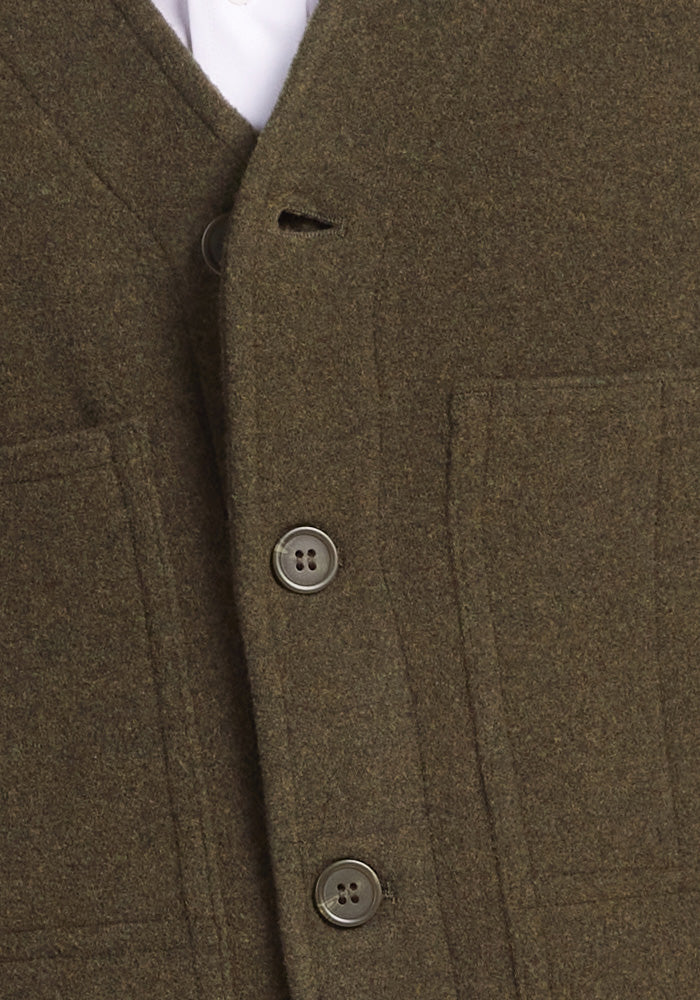 Close-up of the Baker Vest in Dark Forest by Woolx, crafted from boucle knit fabric. It features three brown buttons and two visible pockets, with its textured appearance adding depth. A portion of a white shirt peeks out from underneath.