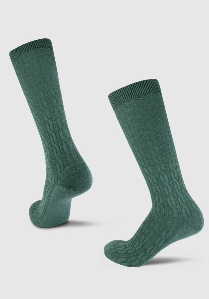 The Tilly Cable Knit Sock in Duck Green from Woolx is showcased against a plain light background, featuring two socks positioned to emphasize their intricate cable pattern and textured design.