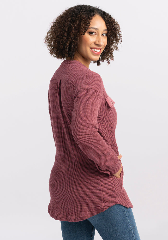 A woman with curly hair wears the Oaklynn Waffle Shacket in Wild Ginger from Woolx, paired with jeans, smiling as she glances over her shoulder against a plain white background.