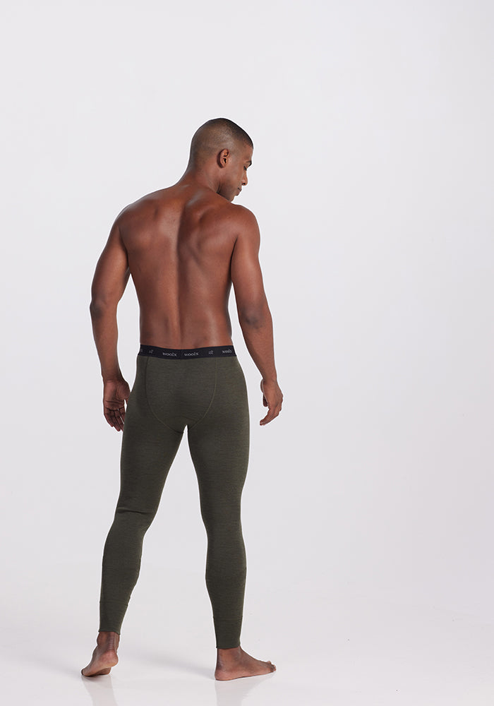 A muscular man with a shaven head stands shirtless, facing away from the camera. He is wearing dark green Backcountry Leggings in Dark Moss, crafted by Woolx from performance fabric ideal for cold weather adventures. The background is plain and white.