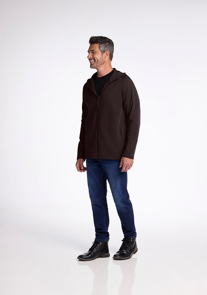 A man stands against a plain white background. He is smiling and looking to his right. He is wearing the Woolx Boulder Hoodie in French Roast, a black t-shirt, blue jeans, and black lace-up boots. His hair is short and neatly styled.