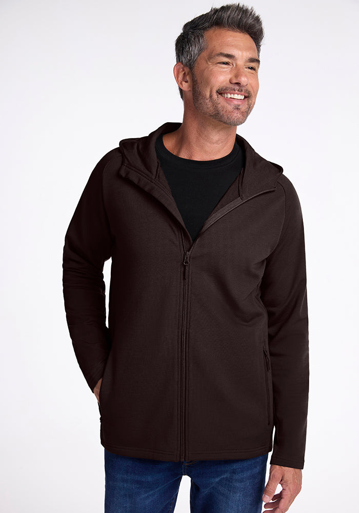 A man with short salt-and-pepper hair smiles, wearing a sport fit, dark brown Boulder Hoodie - French Roast by Woolx over a black shirt and blue jeans. The background is plain white.