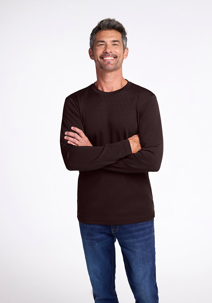 A man with short gray hair and a beard smiles at the camera. He is wearing a black Woolx Easton Shirt and blue jeans. His arms are crossed over his chest, showcasing the midweight shirt perfectly. The background is plain white. 