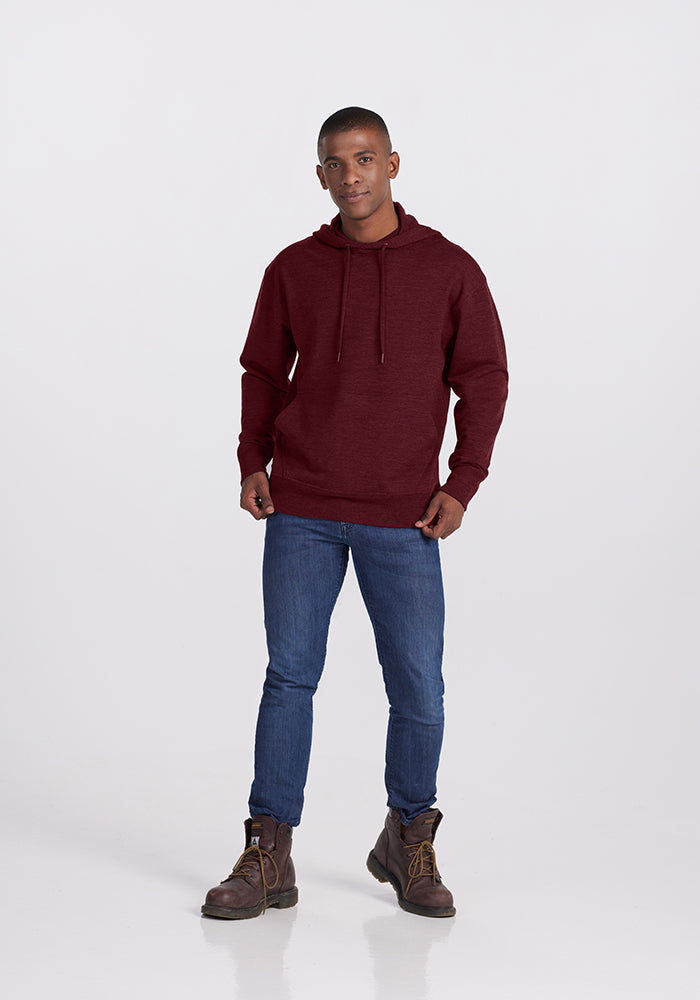 A young man wearing a cranberry melange Woolx Chase hoodie, blue jeans, and brown boots stands against a plain white background. He has a neutral expression with his arms relaxed at his sides.