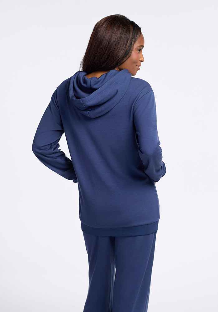 A person with long dark hair is shown from the back wearing a matching navy blue Avery Hoodie - Starry Night by Woolx and Parker sweatpants. The individual stands with their hands resting on their hips against a plain white background.