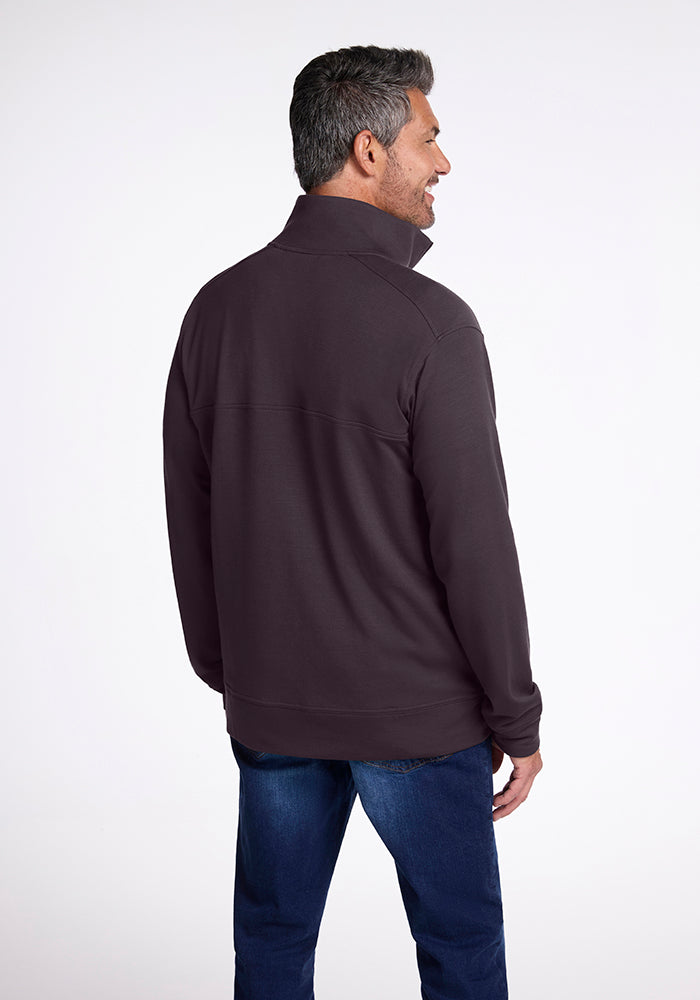 A man in a Chocolate Plum Wool Aire™ Mason by Woolx zip-up jacket and blue jeans stands smiling with his back to the camera. The background is plain and light-colored, showcasing his distinctive WoolAire style.