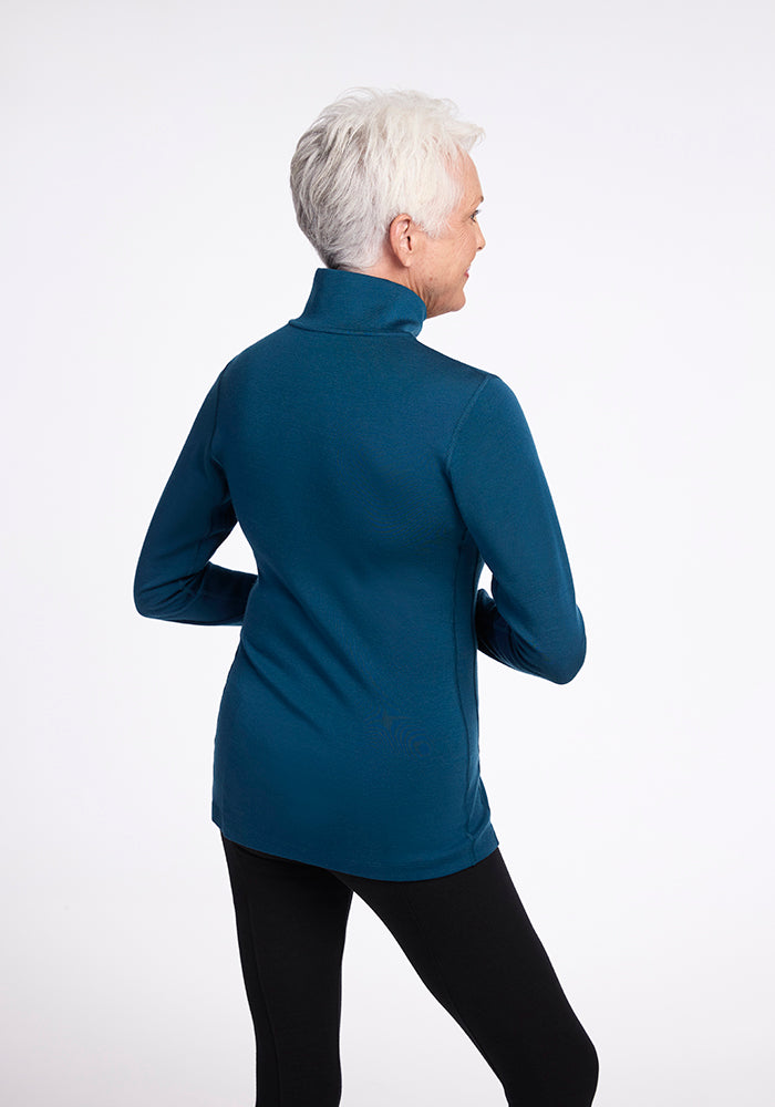 A person with short, white hair is seen from the back, wearing a blue Woolx Brooke 1/4 Zip top and black leggings. They are standing against a plain white background.