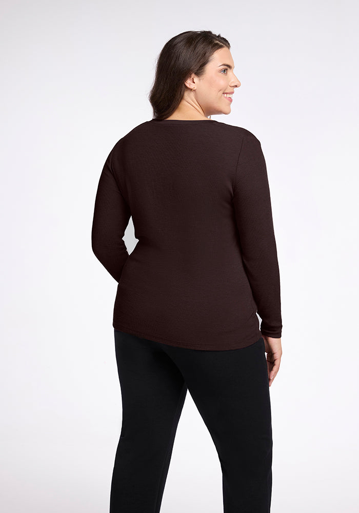 A woman with long dark hair is standing and smiling, wearing a black Reese Ribbed Top by Woolx and black pants. She is shown from the back, slightly turned to the side, against a plain white background.