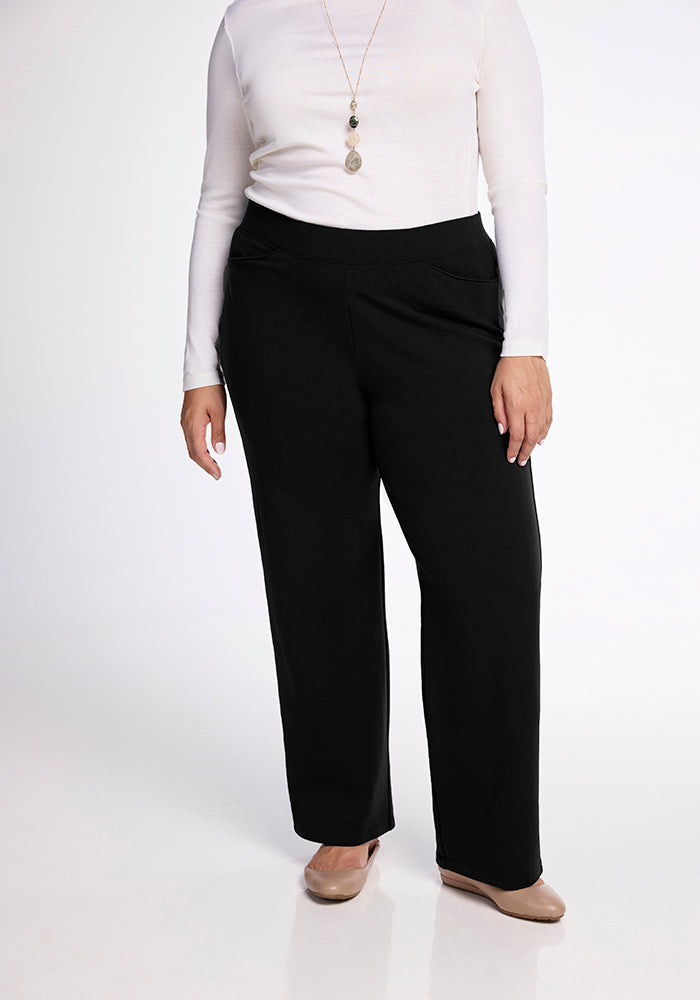 A person wearing a long-sleeve white top, Ellie Pants Tall by Woolx with deep front pockets, and beige shoes. The outfit is accessorized with a long pendant necklace. The image focuses on the clothing, displaying only the lower half of the person's body.