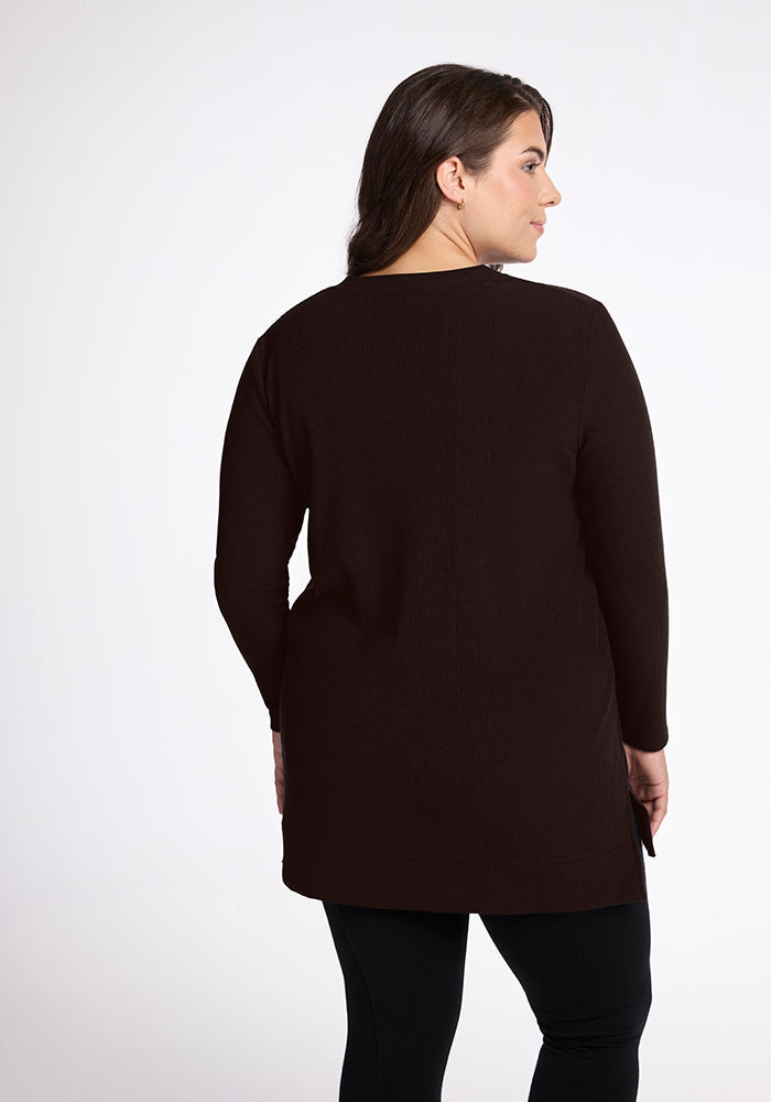 A person with long brown hair is standing with their back to the camera, wearing a long-sleeved Woolx Evie Tunic in French Roast and black leggings against a white background.