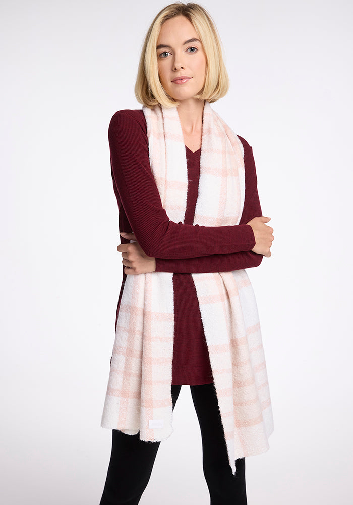 A woman with shoulder-length blonde hair is wearing a burgundy long-sleeve top and a Woolx Bradie Scarf in Mauve Plaid. She is standing with her arms crossed against a plain white background.