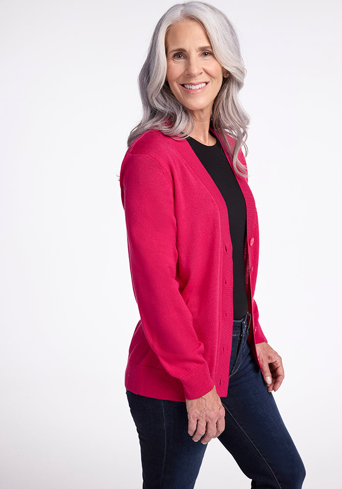 A woman with long, gray hair smiles while wearing the Gia Sweater in Berry Burst from Woolx over a black top. She is standing against a plain white background.