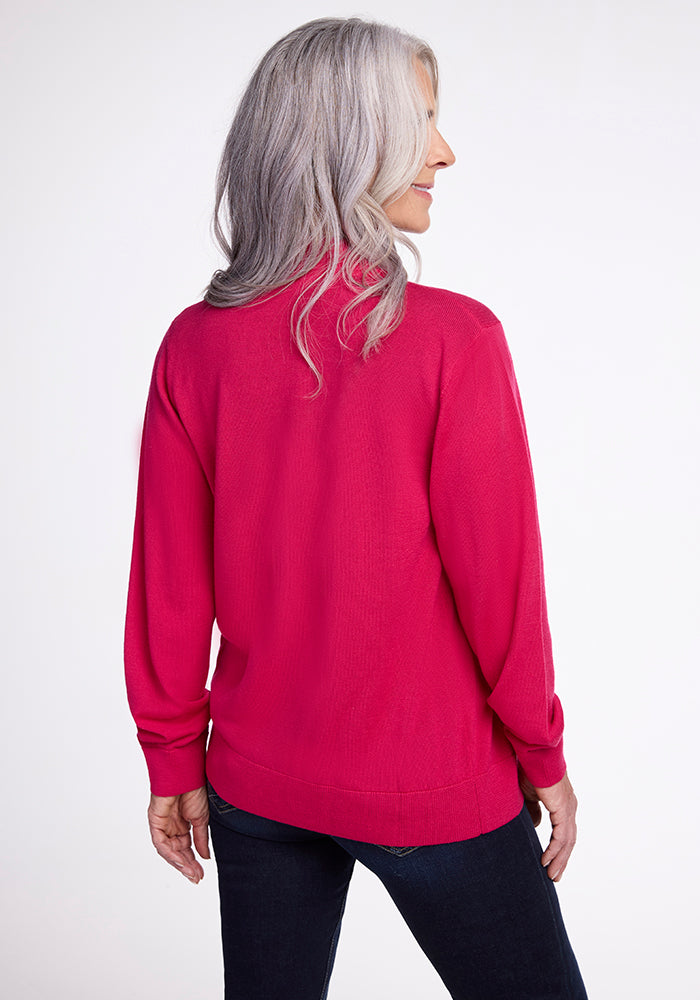 A woman with long grey hair stands facing away from the camera, wearing the Woolx Gia Sweater in Berry Burst and dark jeans. She appears to be looking slightly to the side against a plain white background.