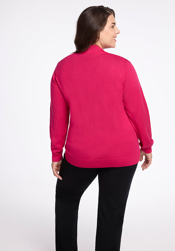 A woman with long dark hair stands facing slightly away from the camera, smiling. She is wearing the Woolx Gia Sweater in Berry Burst and black pants. The background is white, creating a simple and clean setting.