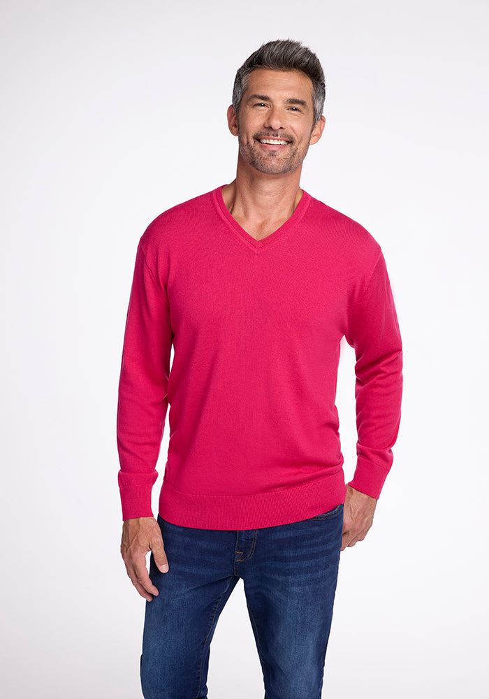 A man with short gray hair smiles while wearing the Vincenzo Sweater in Berry Burst from Woolx, paired with dark blue jeans. He stands against a plain white background with his hands by his sides.