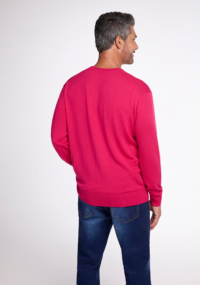 A man with gray hair is standing, facing away from the camera, wearing the Woolx Vincenzo Sweater in Berry Burst paired with dark blue jeans. The background features a plain white studio setting.