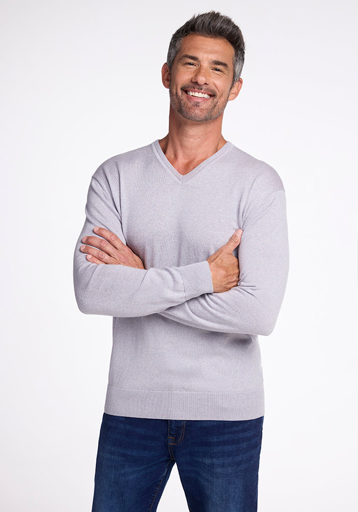 A man with short gray hair and a beard smiles while crossing his arms. He is wearing the Woolx Vincenzo Sweater in Mist paired with blue jeans, standing against a plain white background. 