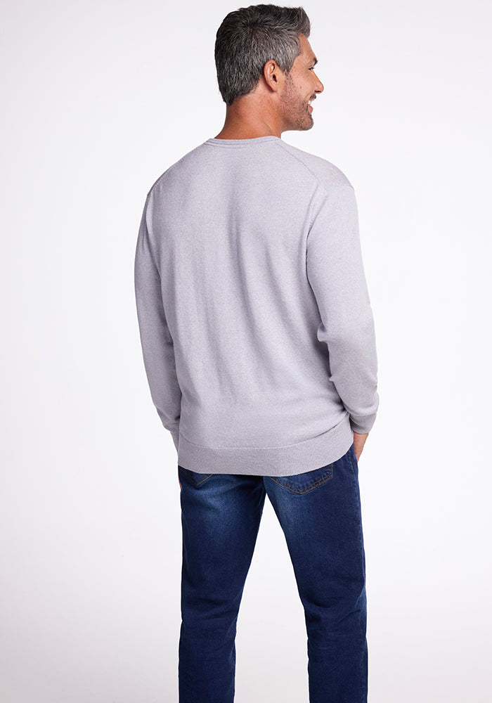 A man with gray hair, dressed in a Vincenzo Sweater - Mist by Woolx and blue jeans, is standing with his back to the camera against a plain white background.