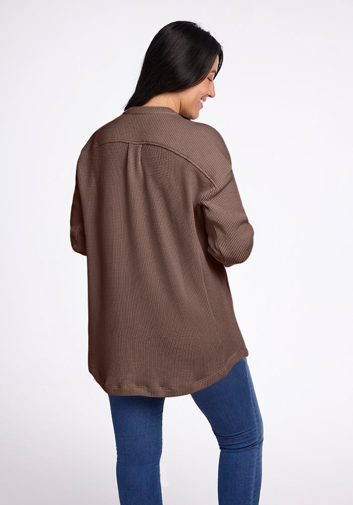 A person with long black hair facing away from the camera is smiling while wearing the Oaklynn Waffle Shacket in Latte by Woolx, paired with blue jeans against a plain white background.