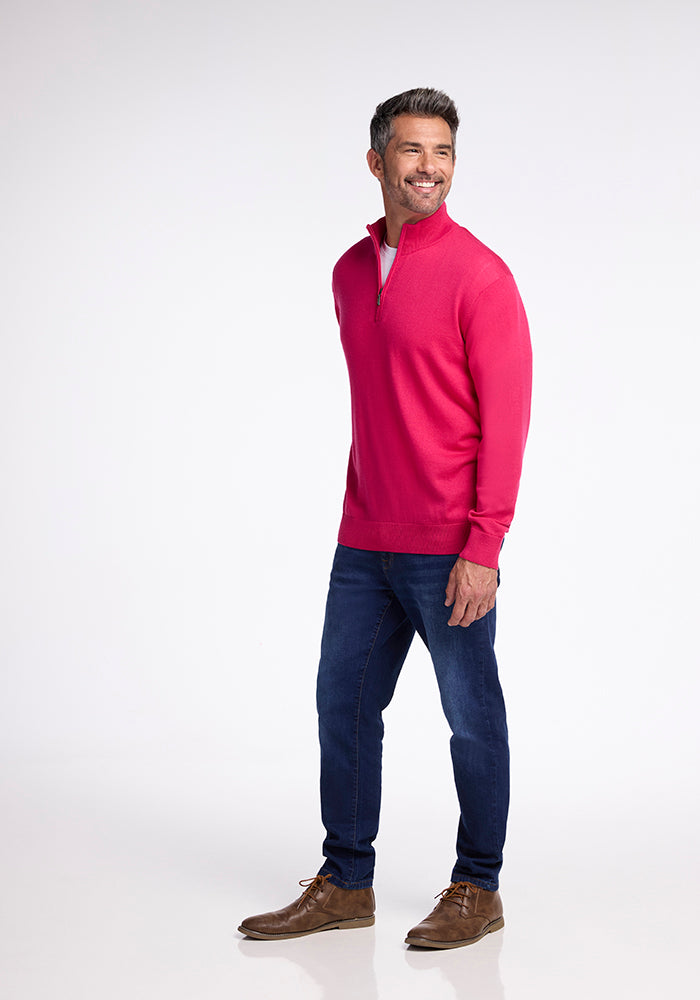 A man stands smiling, wearing the Woolx Enzo Quarter Zip in Berry Burst, paired with blue jeans and brown leather shoes. The plain white background accentuates his casual yet stylish outfit.