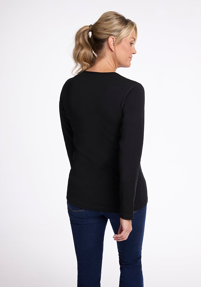 A person with blonde hair in a ponytail is standing and facing away from the camera against a white background, wearing the Riley Long Sleeve Crew by Woolx and blue jeans.