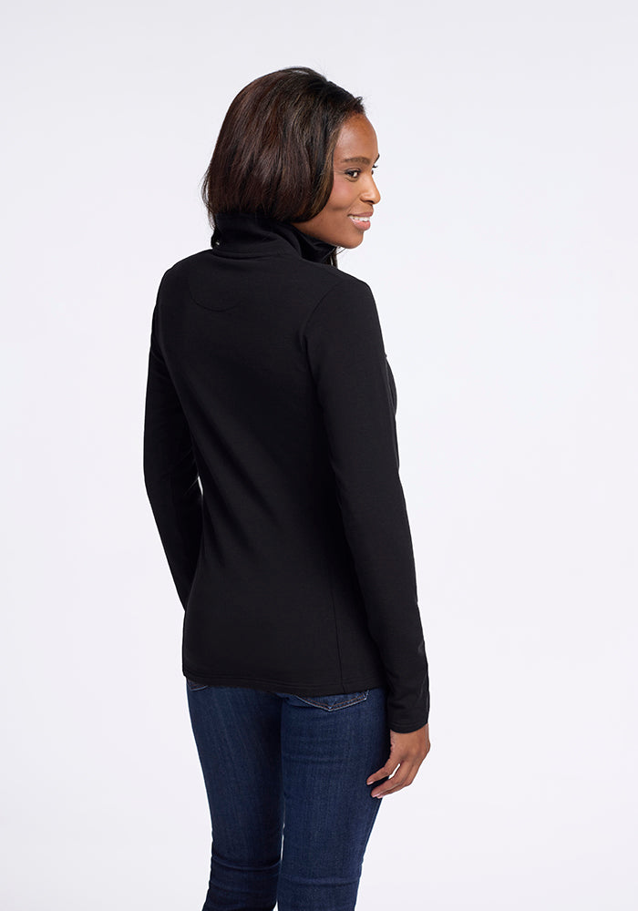 A person with short dark hair is shown from the back, slightly turned to the side, wearing a stylish black Finley Zip Up Sweatshirt by Woolx and blue jeans. They are standing against a plain white background and appear to be smiling, showcasing a flattering look.