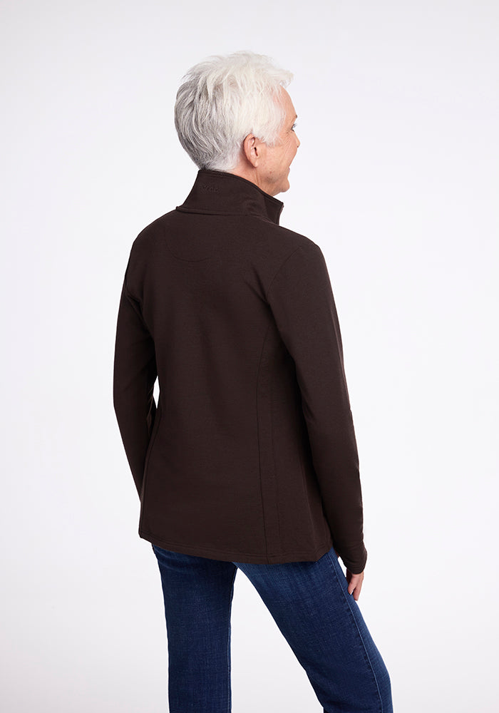 A person with short white hair is standing and facing away from the camera. They are wearing the Woolx Finley Zip Up Sweatshirt in French Roast and blue jeans. The background is a plain, light color.