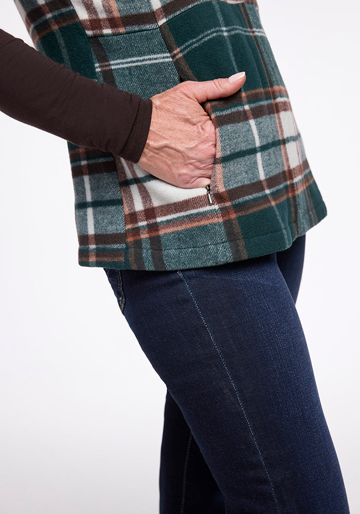 A person with a Woolx Colbie Vest in Espresso Plaid and blue jeans has their right hand in the vest's pocket. The vest features a green, white, brown, and black plaid pattern, and the person is also wearing a long-sleeved black shirt underneath.