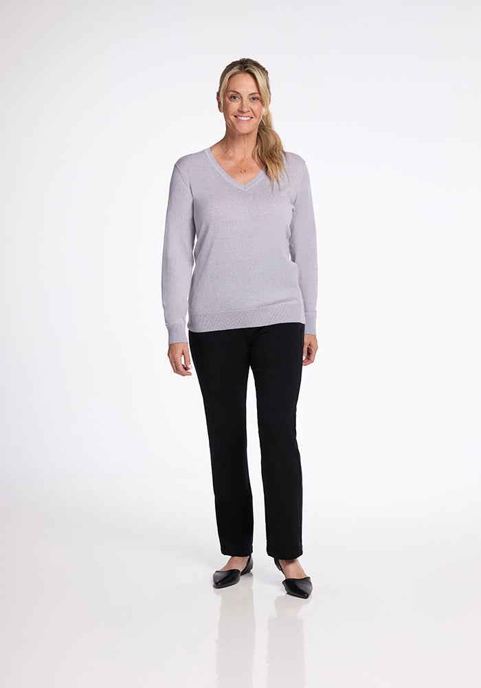 A person is standing against a plain white background. They have long blonde hair tied back and are wearing the light gray Francesca Sweater in mist by Woolx, paired with black pants and black flats. They are smiling and have a relaxed posture.