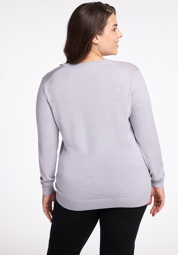 A person with long brown hair stands facing away from the camera, wearing the Francesca Sweater in Mist by Woolx and black pants against a white background.