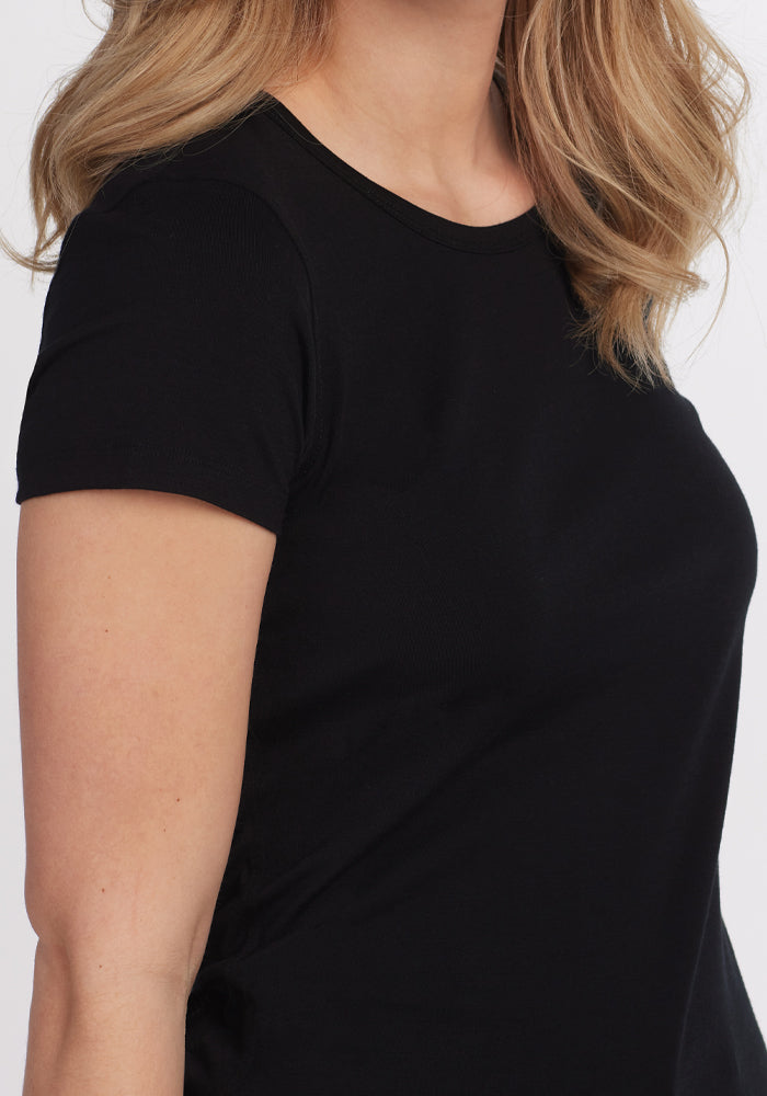 A person with long, wavy hair is wearing the Addie Short Sleeve Crew - Black by Woolx. The image highlights the upper torso and shoulder area against a neutral background, emphasizing the Woolmark® Certified fabric recognized for its odor-free properties.